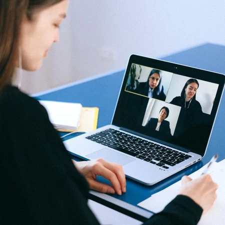 A smart-dressed woman sitting at a desk with a laptop, having a videoconference with three other colleagues