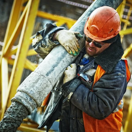A man in hi-viz jacket pouring concrete out of a big tube that he holds over his shoulder