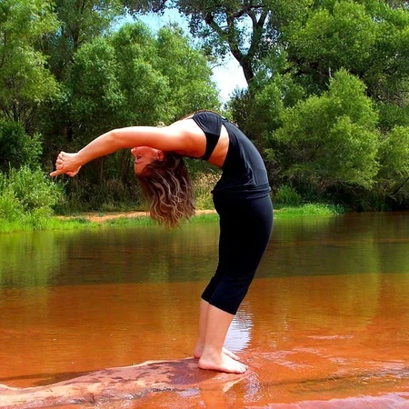 A woman bending backwards doing yoga next to lake
