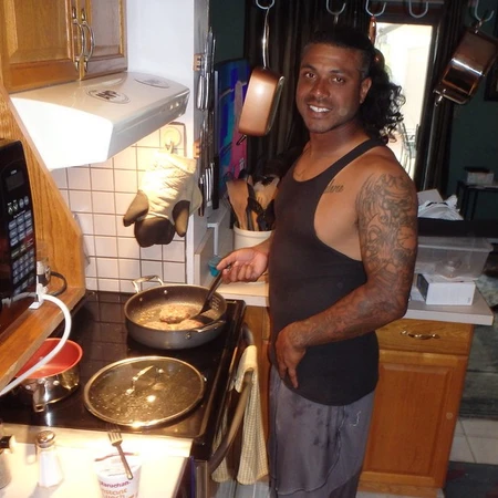A young man in the kitchen is frying meat, dressed in a black tank-top