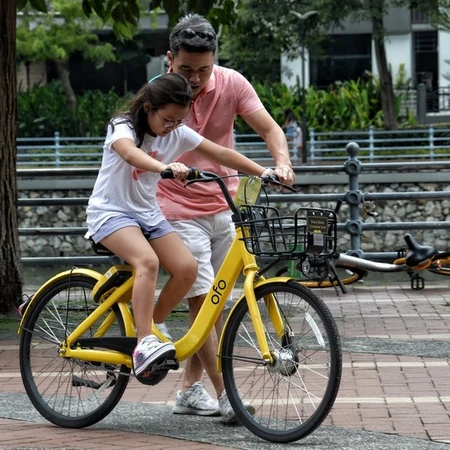 A man teaching a girl to ride a yellow bike, helping her keep the balance