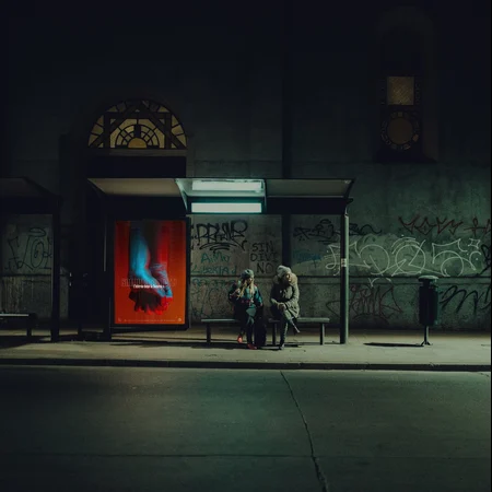 Two people at a bus stop waiting for a late night bus