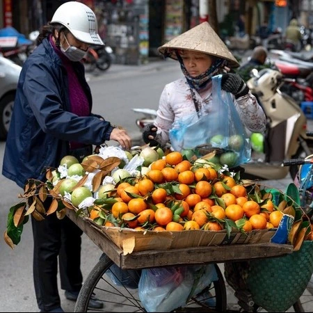 Two people in the street buying oranges from a cart used by a street vendor